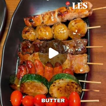 A long black plate of grilled skewers: chicken, scallops, bacon-wrapped pieces, courgette and cherry tomatoes.